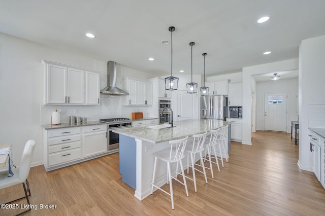 kitchen with appliances with stainless steel finishes, light wood-type flooring, white cabinets, and wall chimney exhaust hood