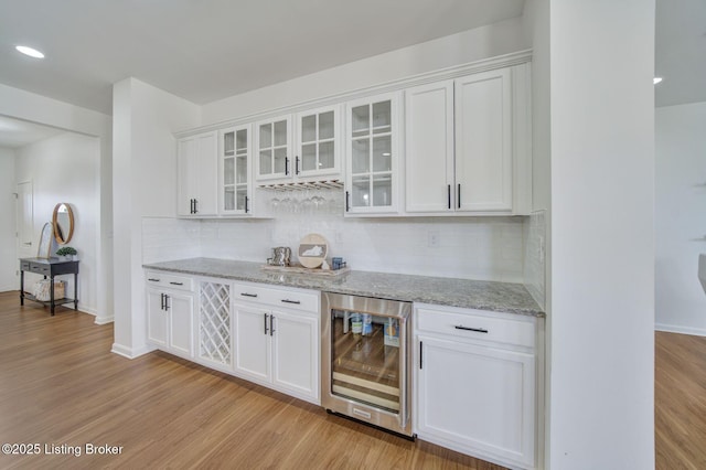 bar with beverage cooler, a bar, light wood finished floors, and backsplash