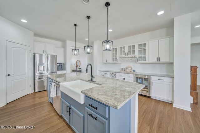 kitchen with appliances with stainless steel finishes, wine cooler, a sink, and light wood-style flooring