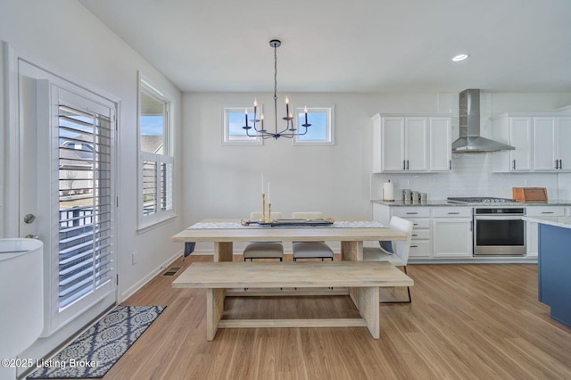 kitchen with stainless steel appliances, white cabinets, wall chimney range hood, and light wood finished floors