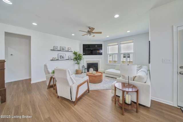 living room featuring a glass covered fireplace, baseboards, recessed lighting, and wood finished floors