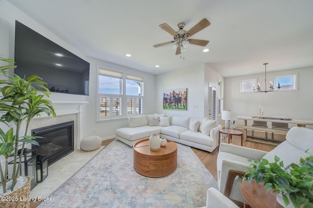 living room with ceiling fan with notable chandelier, baseboards, a tile fireplace, and recessed lighting