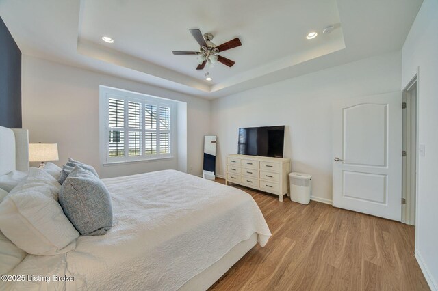 bedroom with light wood-style flooring, a tray ceiling, and baseboards