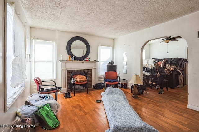 interior space with a brick fireplace, a textured ceiling, arched walkways, and wood finished floors