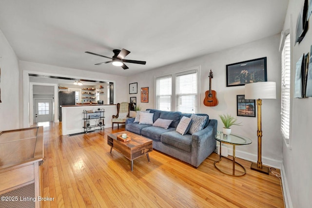 living area featuring a ceiling fan, baseboards, a healthy amount of sunlight, and light wood finished floors