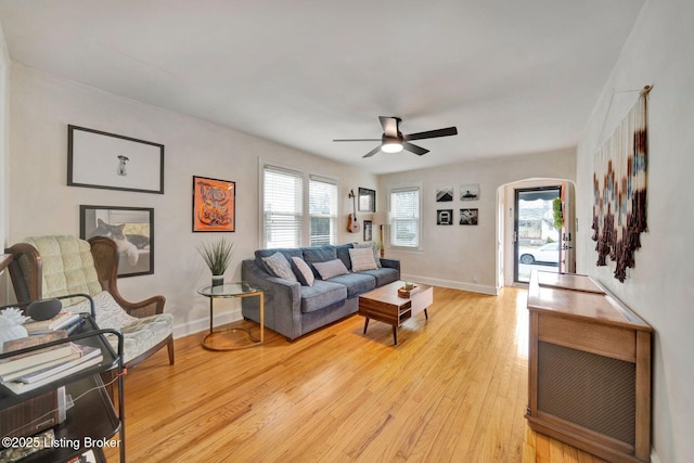 living room featuring a healthy amount of sunlight, light wood-style floors, baseboards, and arched walkways