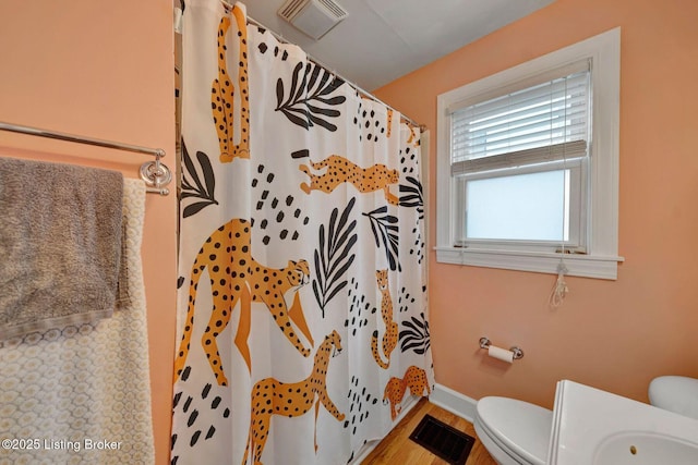 bathroom with toilet, a shower with curtain, visible vents, and wood finished floors