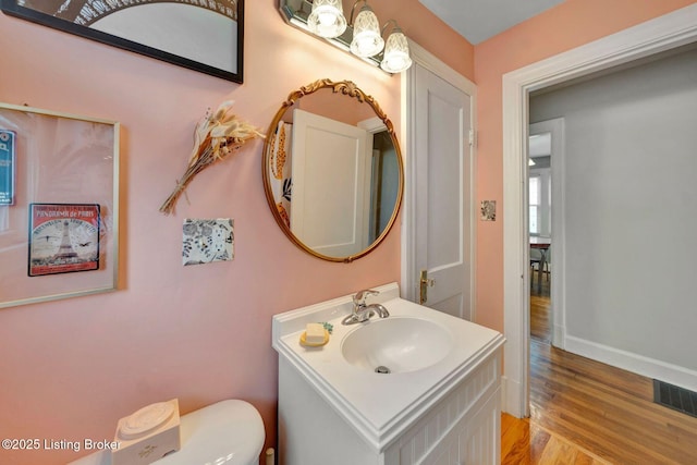 half bathroom with visible vents, toilet, vanity, wood finished floors, and baseboards