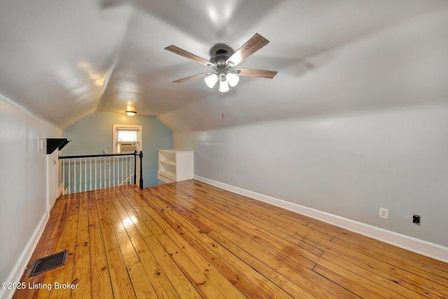 additional living space featuring a ceiling fan, visible vents, vaulted ceiling, baseboards, and hardwood / wood-style floors