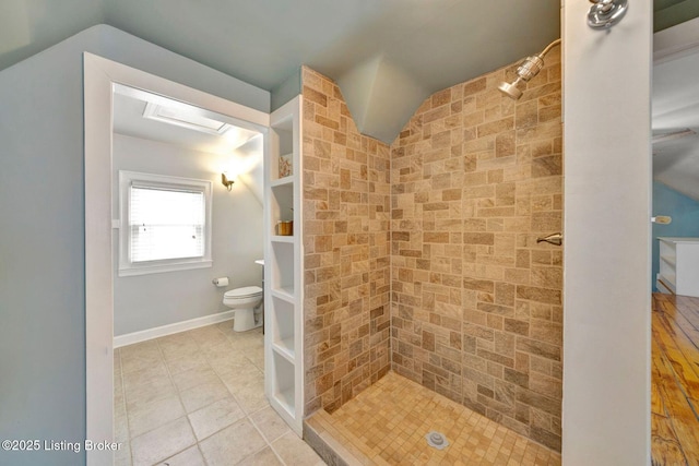 full bath with lofted ceiling, toilet, tiled shower, baseboards, and tile patterned floors