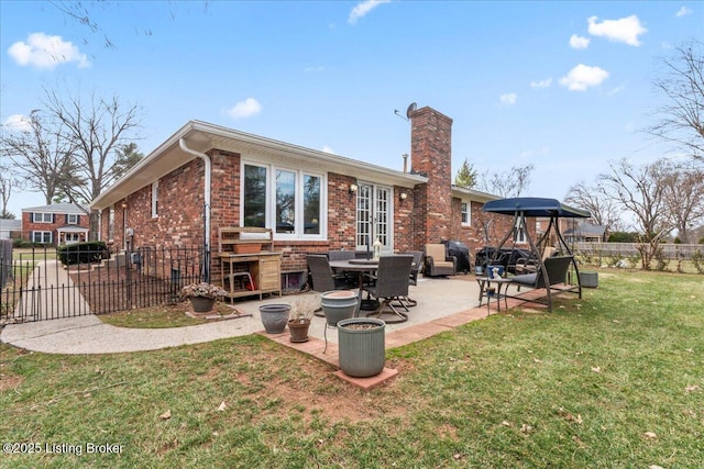 back of house featuring a patio, brick siding, fence, a lawn, and a chimney