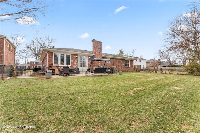 back of property featuring a fenced backyard, a chimney, a lawn, and brick siding