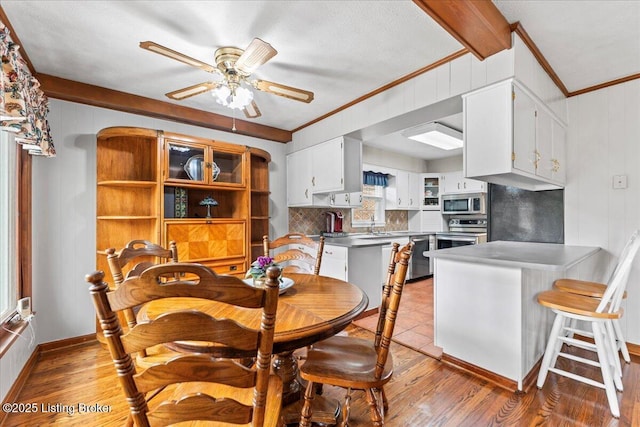 dining space with arched walkways, light wood-style flooring, a ceiling fan, baseboards, and ornamental molding