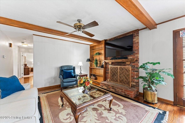 living room with a brick fireplace, ceiling fan, wood finished floors, beamed ceiling, and baseboards