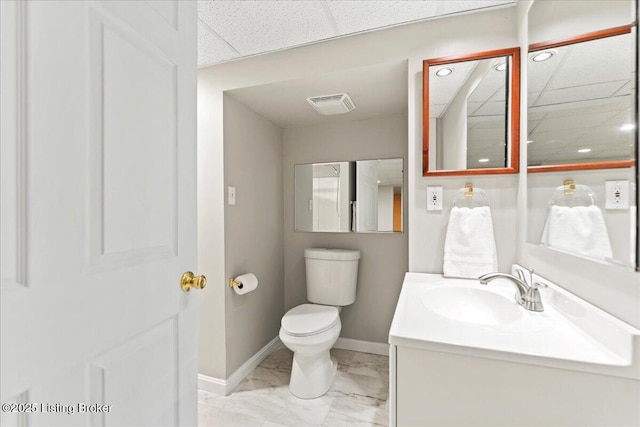 bathroom with visible vents, toilet, vanity, a drop ceiling, and baseboards