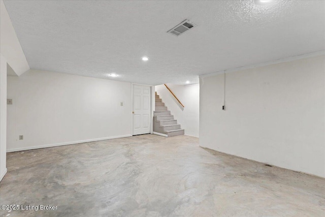 finished basement with stairway, visible vents, and a textured ceiling