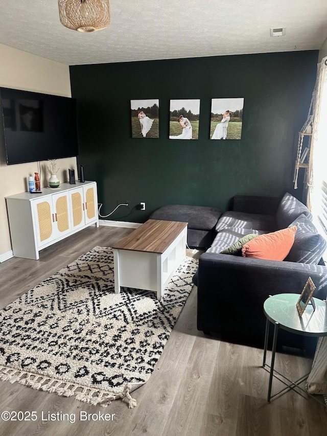 living area with visible vents, baseboards, a textured ceiling, and wood finished floors