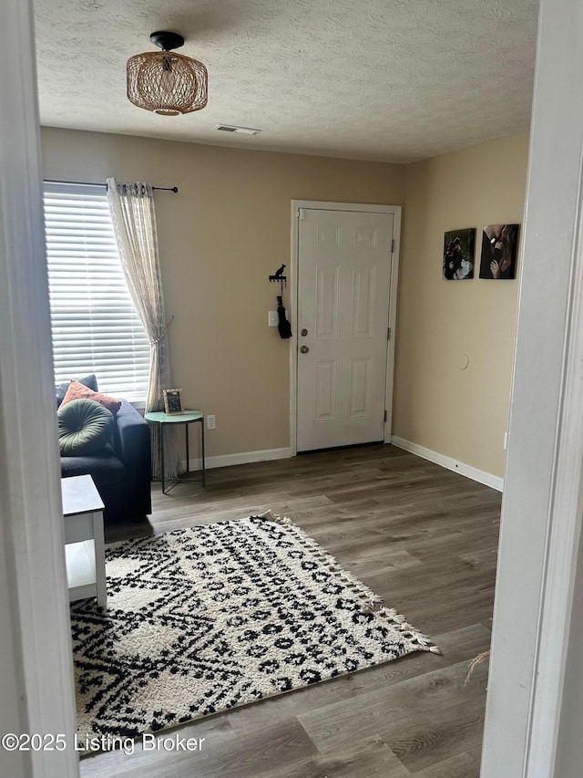 entrance foyer with baseboards, wood finished floors, visible vents, and a textured ceiling