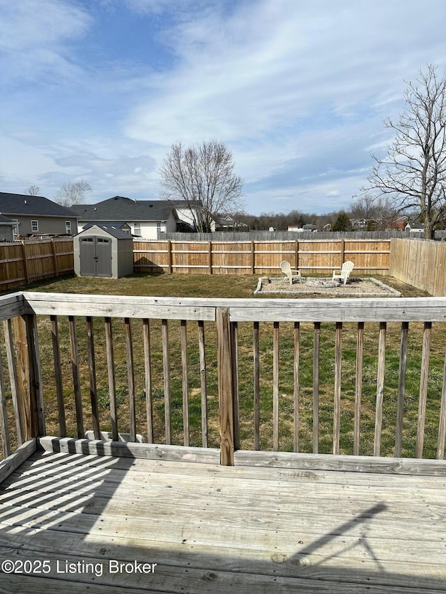 wooden terrace featuring a fenced backyard, an outdoor fire pit, an outdoor structure, and a shed