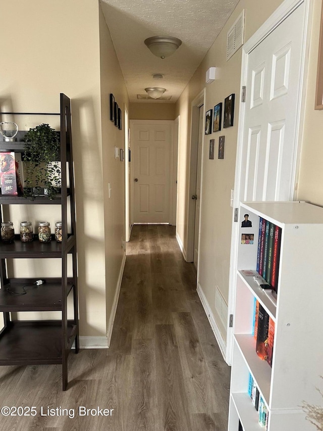 corridor with baseboards, wood finished floors, visible vents, and a textured ceiling