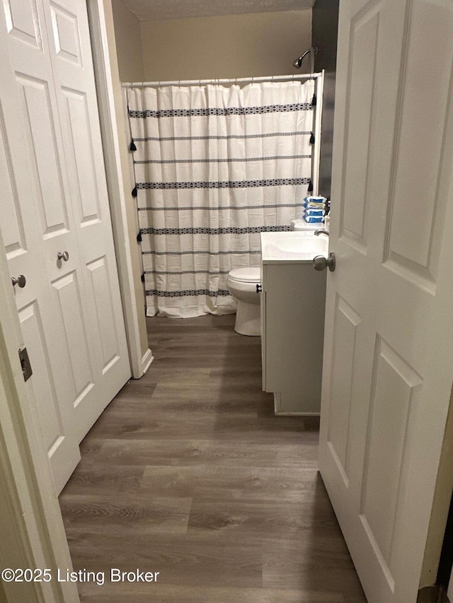 full bath featuring a shower with shower curtain, toilet, wood finished floors, and vanity