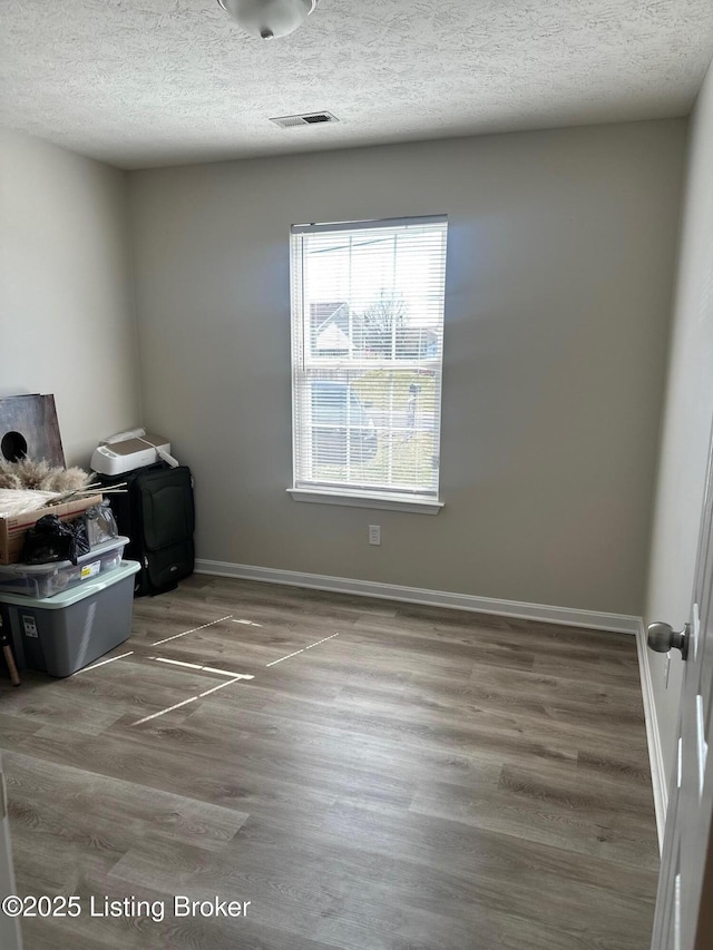 empty room featuring a textured ceiling, wood finished floors, visible vents, and baseboards