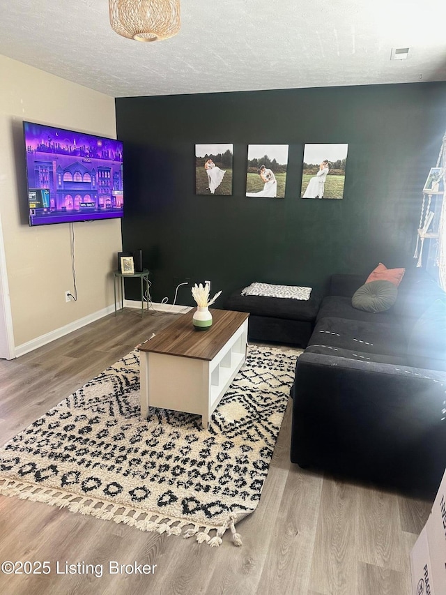 living room featuring visible vents, a textured ceiling, baseboards, and wood finished floors