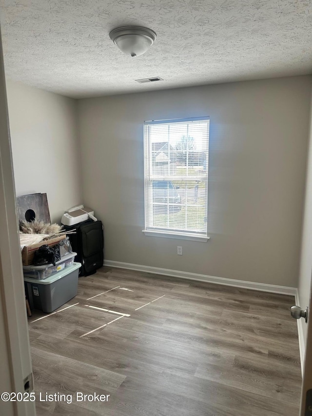 unfurnished room with visible vents, baseboards, a textured ceiling, and wood finished floors