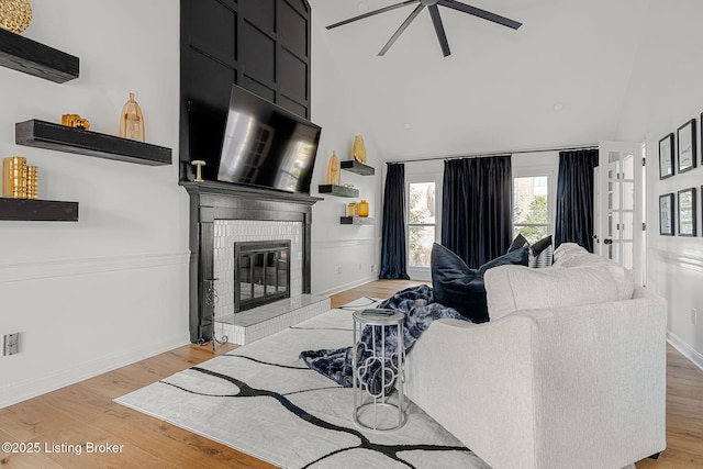 living room with light wood finished floors, baseboards, a ceiling fan, a fireplace, and high vaulted ceiling