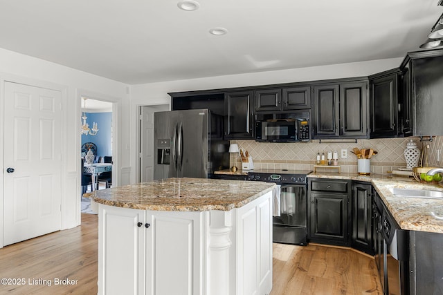 kitchen with dark cabinetry, a sink, light wood finished floors, and black appliances