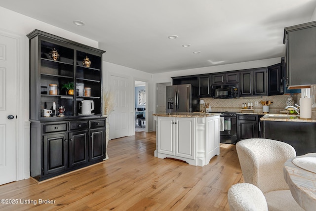 kitchen with a center island, tasteful backsplash, light wood-style flooring, dark cabinetry, and black appliances