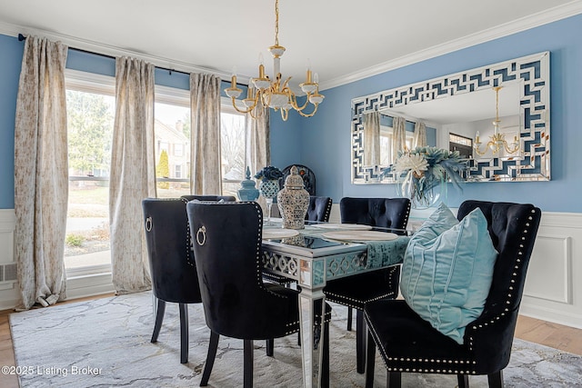 dining area with wainscoting, ornamental molding, wood finished floors, an inviting chandelier, and a decorative wall