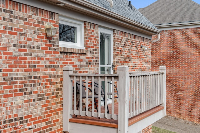 exterior space with a shingled roof, brick siding, and a deck