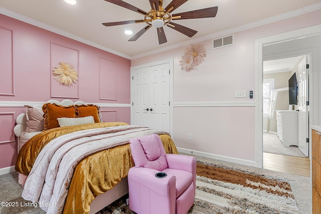 bedroom with ceiling fan, a decorative wall, visible vents, a closet, and crown molding