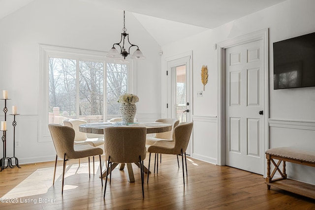 dining room featuring an inviting chandelier, vaulted ceiling, hardwood / wood-style floors, and a decorative wall