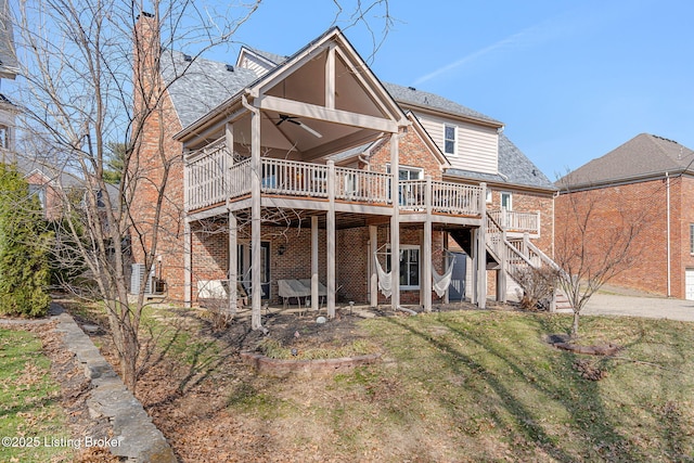 view of front of home with brick siding, a wooden deck, a ceiling fan, a front lawn, and stairs