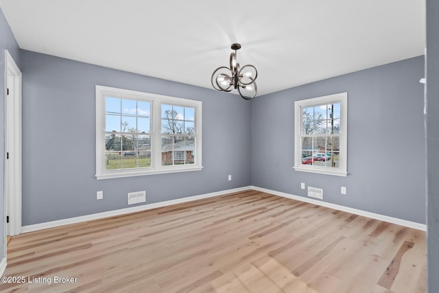 spare room featuring a notable chandelier, wood finished floors, visible vents, and baseboards