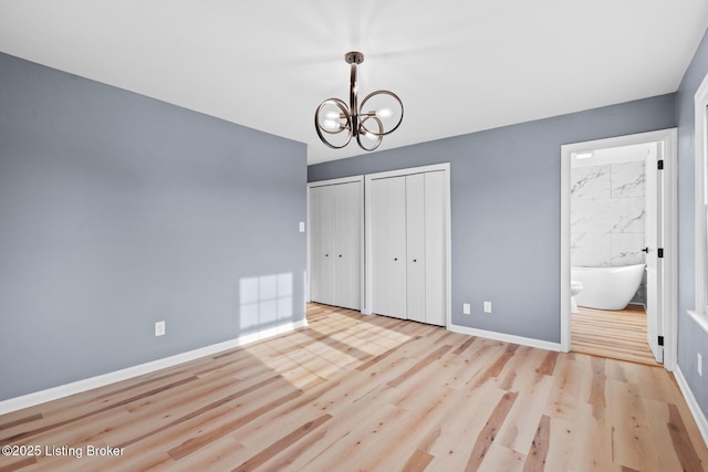 unfurnished bedroom with multiple closets, a notable chandelier, baseboards, and wood finished floors