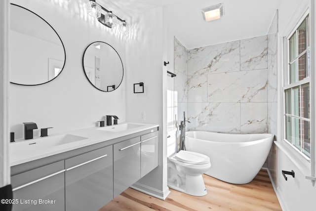 full bathroom featuring a soaking tub, visible vents, a sink, and wood finished floors