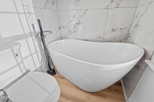 bathroom featuring toilet, a freestanding tub, and wood finished floors