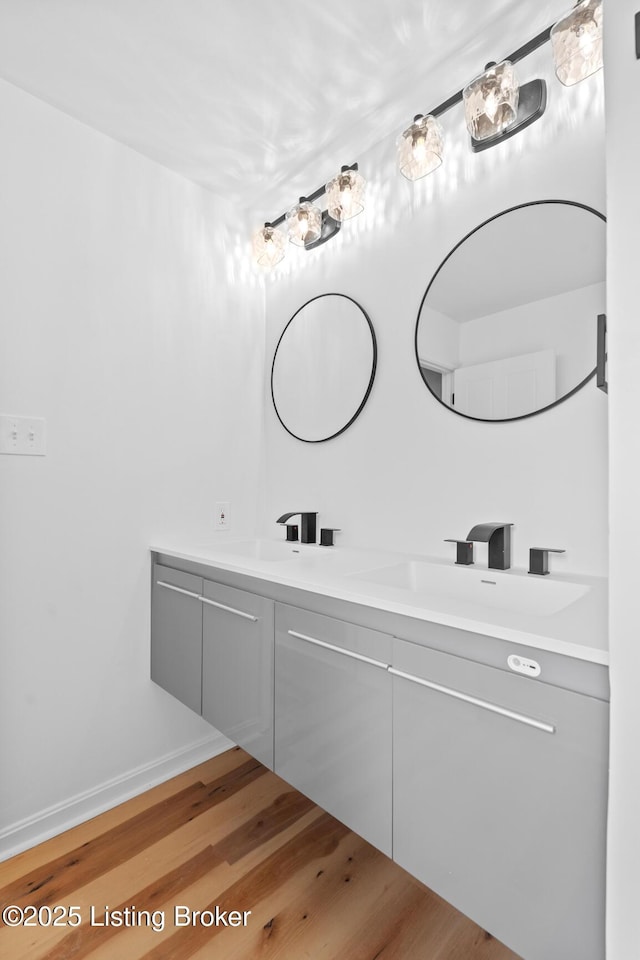 bathroom featuring double vanity, baseboards, a sink, and wood finished floors