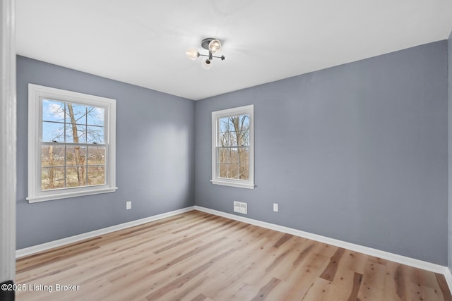 spare room with wood finished floors, visible vents, and baseboards