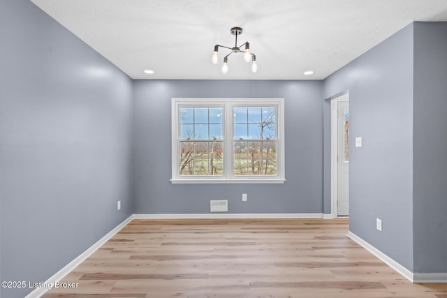 unfurnished dining area with visible vents, light wood finished floors, baseboards, and an inviting chandelier