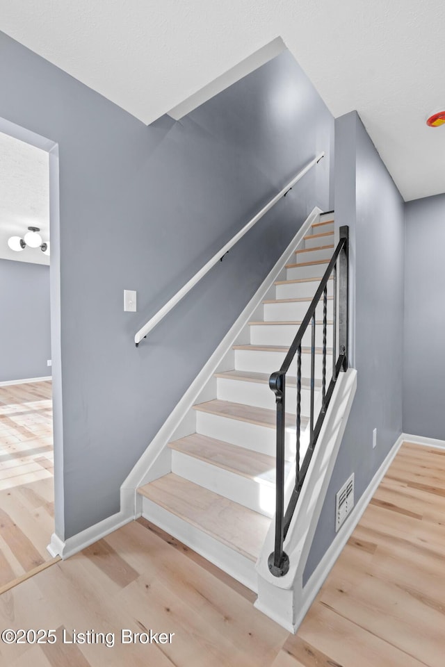 stairway featuring wood finished floors, visible vents, and baseboards