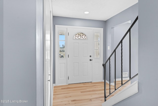 foyer entrance featuring baseboards, stairway, and light wood-style floors