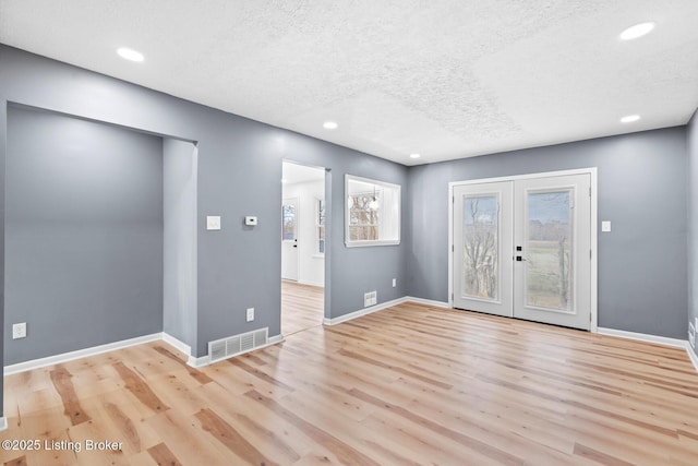 empty room featuring visible vents, a textured ceiling, baseboards, and wood finished floors