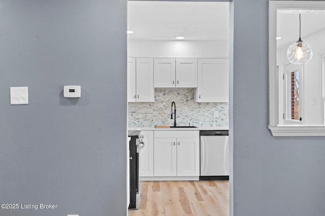 kitchen with stainless steel appliances, a sink, white cabinetry, light countertops, and backsplash