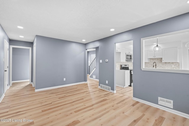 spare room featuring light wood-type flooring, visible vents, baseboards, and stairs