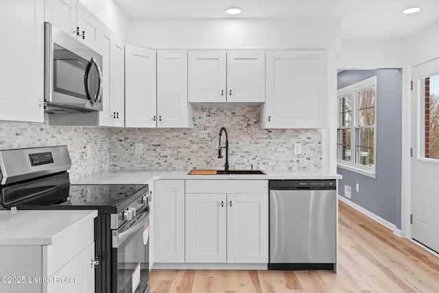 kitchen featuring white cabinetry, stainless steel appliances, a sink, and light countertops