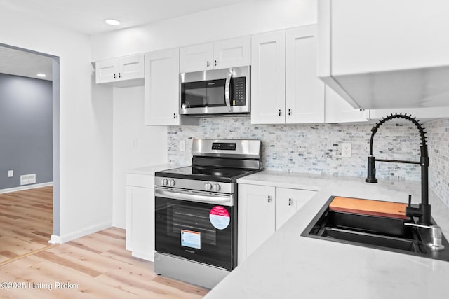 kitchen with white cabinets, appliances with stainless steel finishes, a sink, light countertops, and backsplash